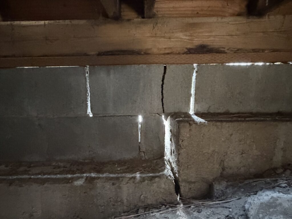 Close-up of a cracked cinder block support pier with deck framing bearing directly on top before repair