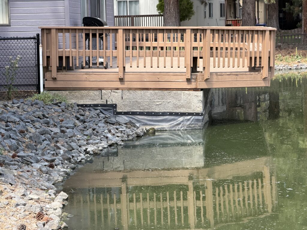 Wide view of the pondside deck showing a cracked support pier at the base before repair