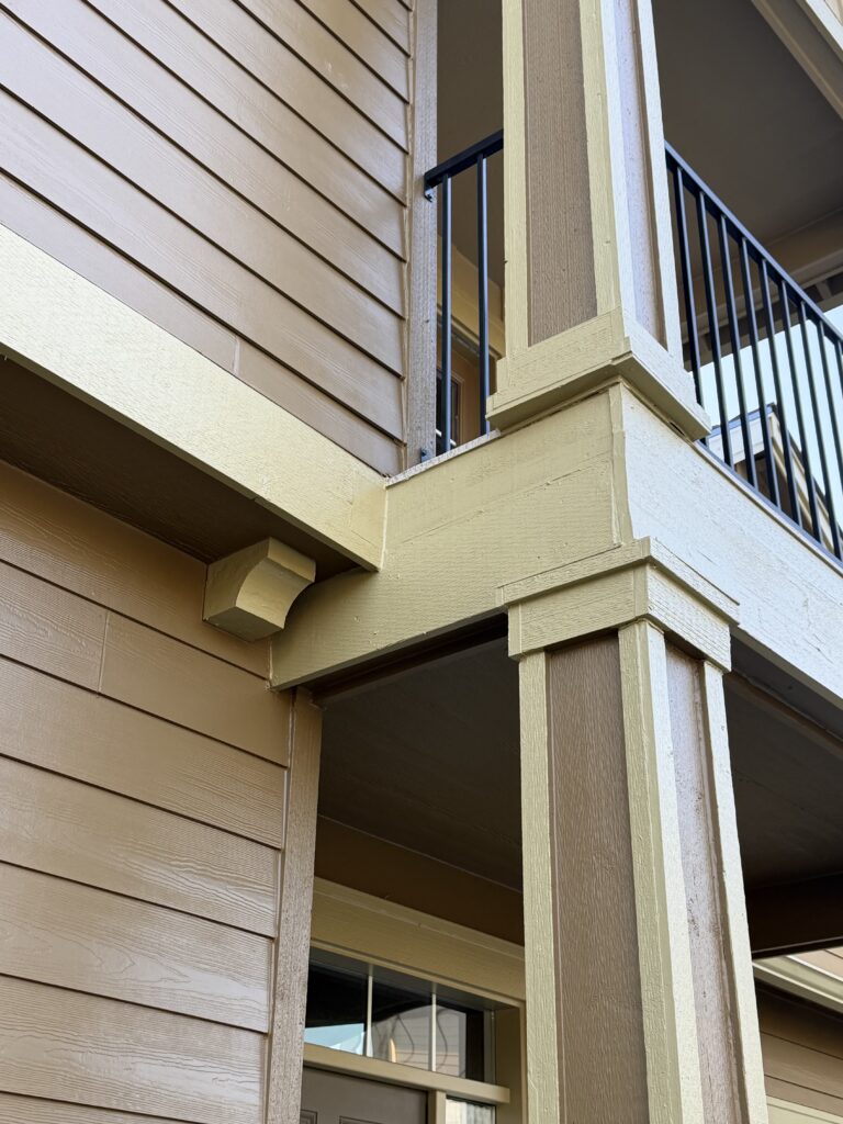 Close-up of painted siding, trim, and black metal balcony railing after repaint