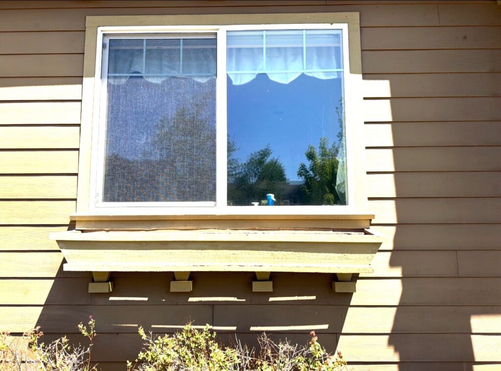 Close-up of second-story window trim and siding before repainting, showing weathered paint